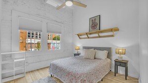 A bedroom with a bed, two bedside tables with lamps, a wooden shelf, a window with blinds, and a ceiling fan. - The Dawg Walk Downtown (Athens)