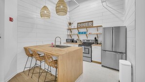 A modern kitchen with a wooden island, wicker chairs, a stainless steel refrigerator, and a sign labeled 'DINER'. - The Dawg Walk Downtown (Athens)