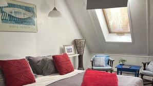 Een slaapkamer met een groot bed, dakraam, een lijst met foto en een bijzettafeltje met een plant.