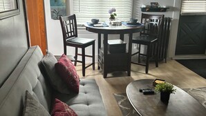 Een woonkamer met een grijze bank, een bijzettafeltje en een eethoek met een tafel en stoelen.