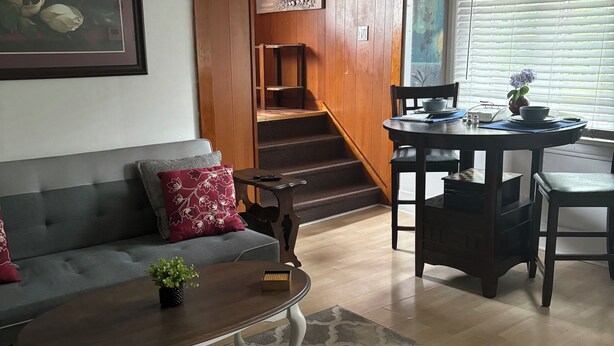 Een woonkamer met een bank, salontafel en een trap naar een eetgedeelte.