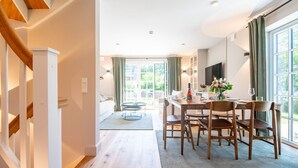 Un espace de repas moderne avec une table et des chaises en bois, un canapé et une vue sur l’extérieur grâce à de grandes fenêtres.