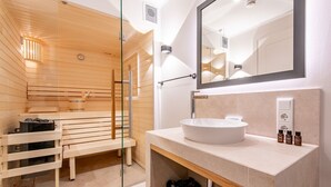 Une salle de bain moderne avec un sauna à parois de verre, un lavabo blanc et un miroir au-dessus.