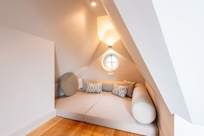 Une chambre confortable située sous les toits, avec un plafond en pente, une fenêtre ronde et un canapé intégré doté de coussins.