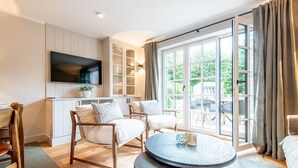 A modern living room with a TV, seating, and a large window. - Landhaus Senwai 3 - Neubau. Stadtnah. Wellness (Sylt)