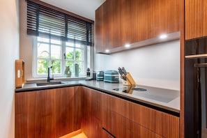 Une cuisine moderne avec des meubles en bois, un four encastré et une fenêtre équipée de stores.