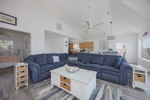 A modern living room with a sectional sofa, a white coffee table, and a dining area in the background.