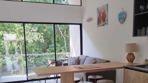 A modern kitchen with a wooden countertop and stools, large windows with a view of greenery, and a dining area with a sofa and chairs. - Modern Family - sized  2 bedroom 2 bath condo just  10 min walk to the beach (Puntarenas Province)