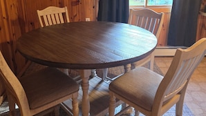 A wooden dining table with four chairs, surrounded by wooden walls and a window with curtains. - Lake front suite on very desirable lake in Gwinn, Mi. Year round activities. (Gwinn)