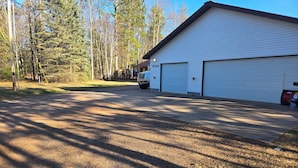 A building with two garage doors, a parked truck, and a forested area in the background. - Lake front suite on very desirable lake in Gwinn, Mi. Year round activities. (Gwinn)
