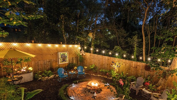A backyard with a fire pit, wooden deck, and string lights.