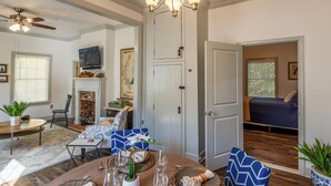 A spacious living room with a fireplace, a dining area with a round table, and a bedroom visible through an open door.