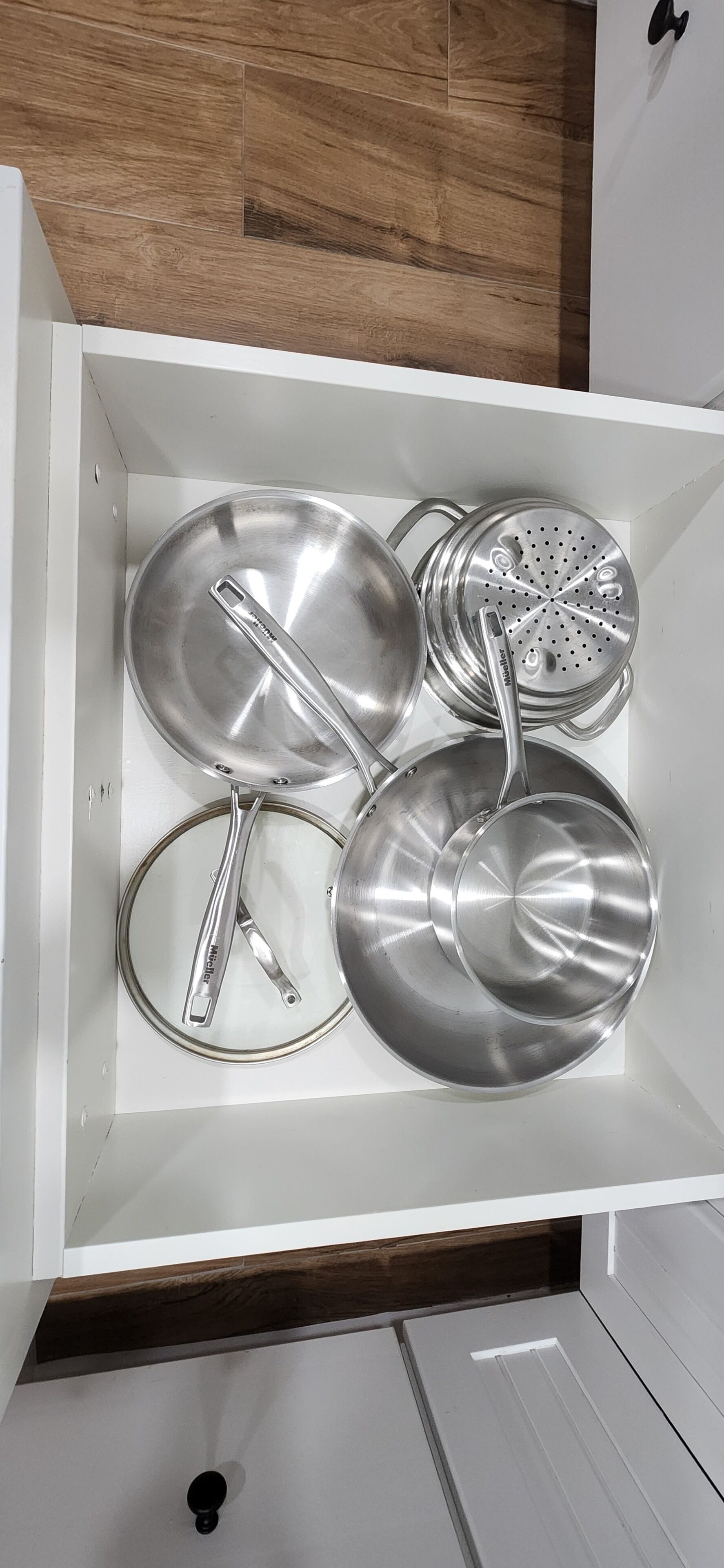 Uma gaveta de cozinha com utensílios de aço inoxidável, incluindo panelas, frigideiras e um escorredor.