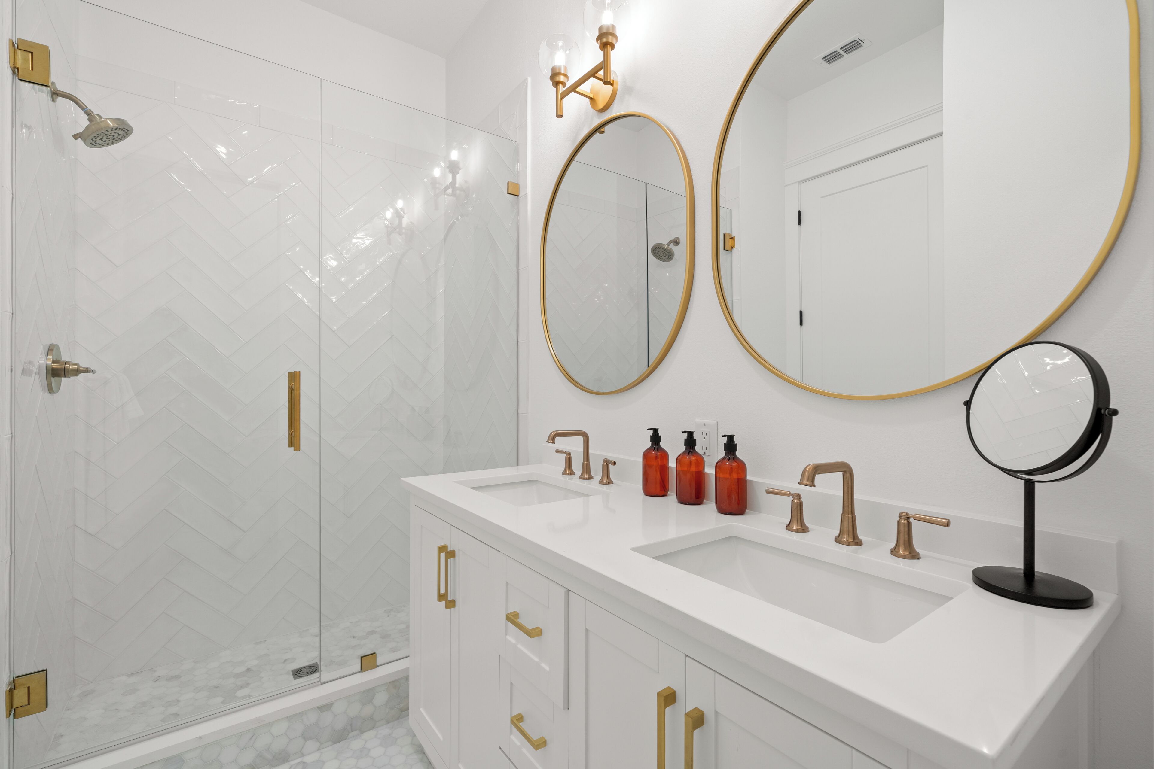 Une salle de bain moderne avec une douche à parois de verre, un meuble-lavabo blanc doté de poignées dorées et deux grands miroirs.
