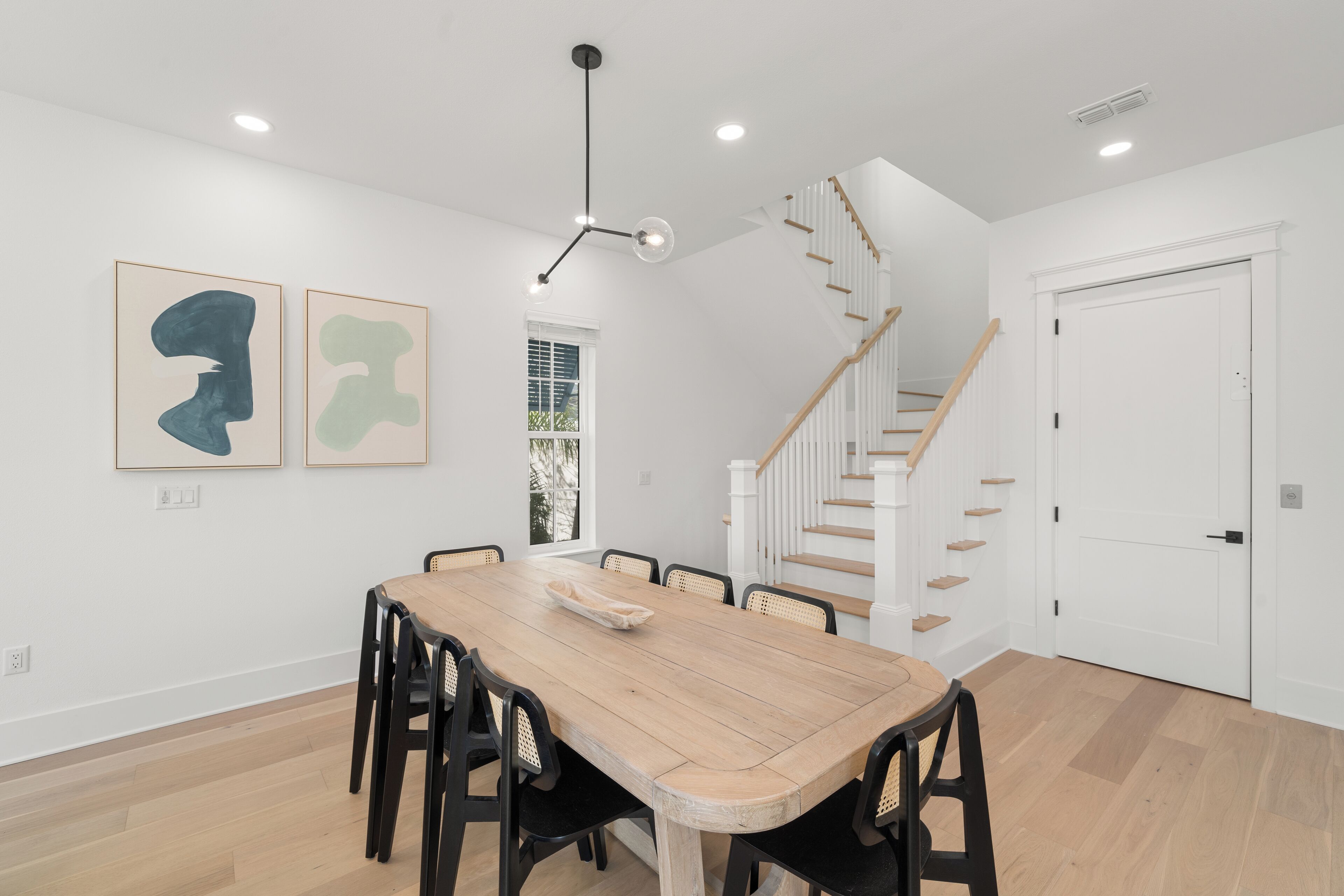 Un comedor con mesa y sillas de madera, una escalera y una puerta blanca.