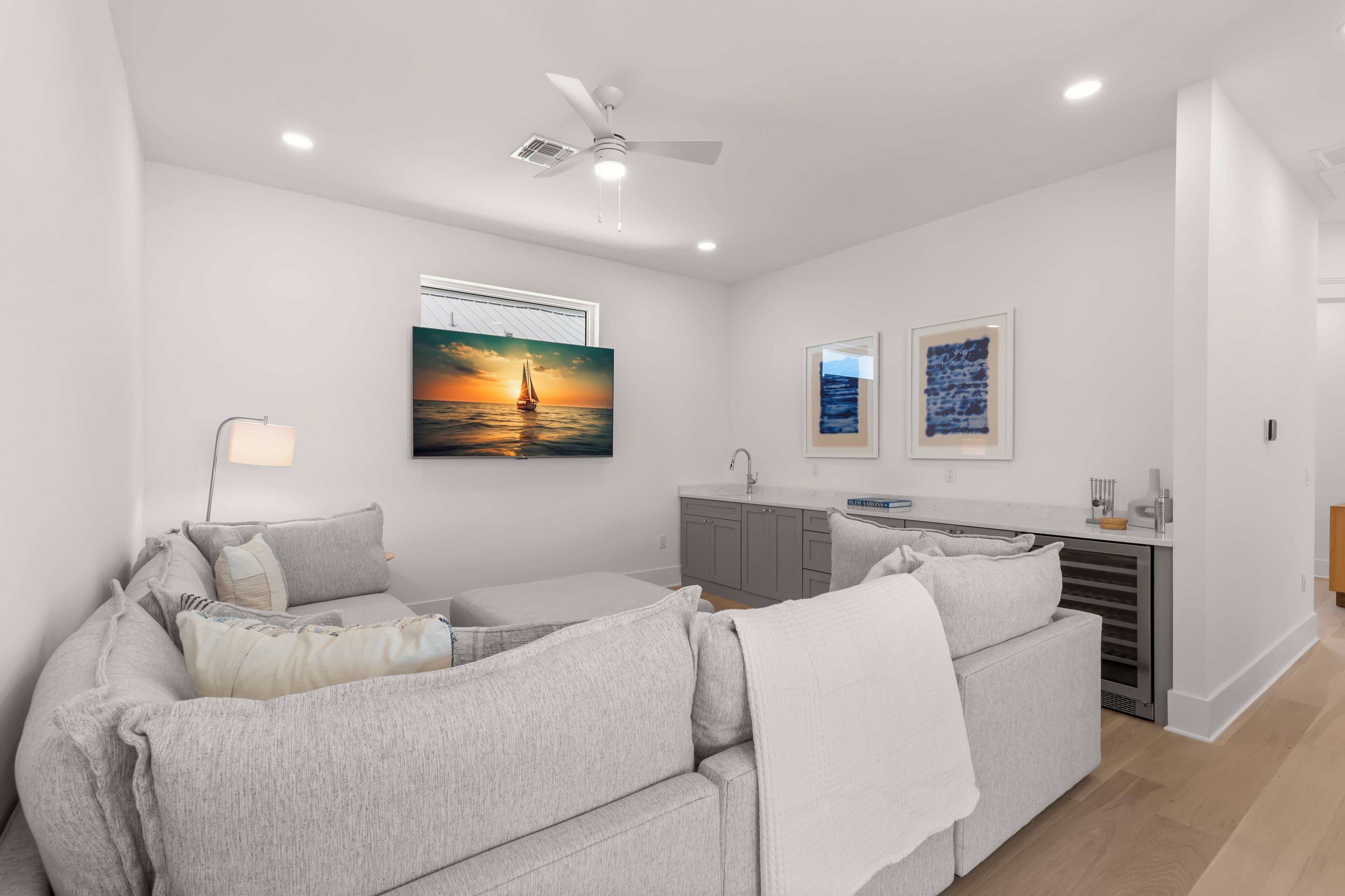 A modern living room with a grey sofa, a ceiling fan, and artwork on the walls.
