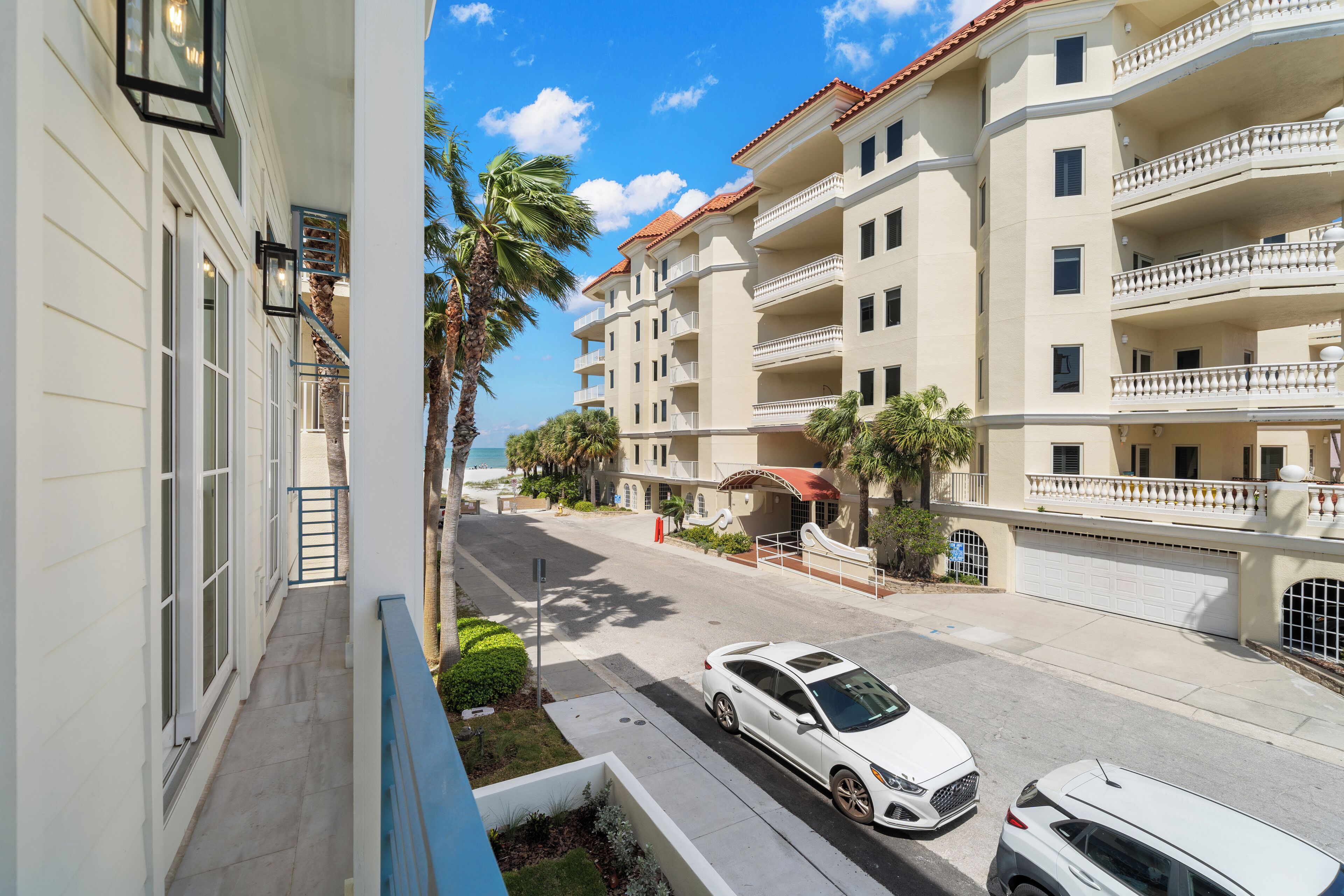 Un edificio residencial de varios pisos con balcones, un área de estar al aire libre techada y vista a la calle con coches estacionados.