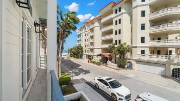 Un edificio residencial de varios pisos con balcones, un área de estar al aire libre techada y vista a la calle con coches estacionados.