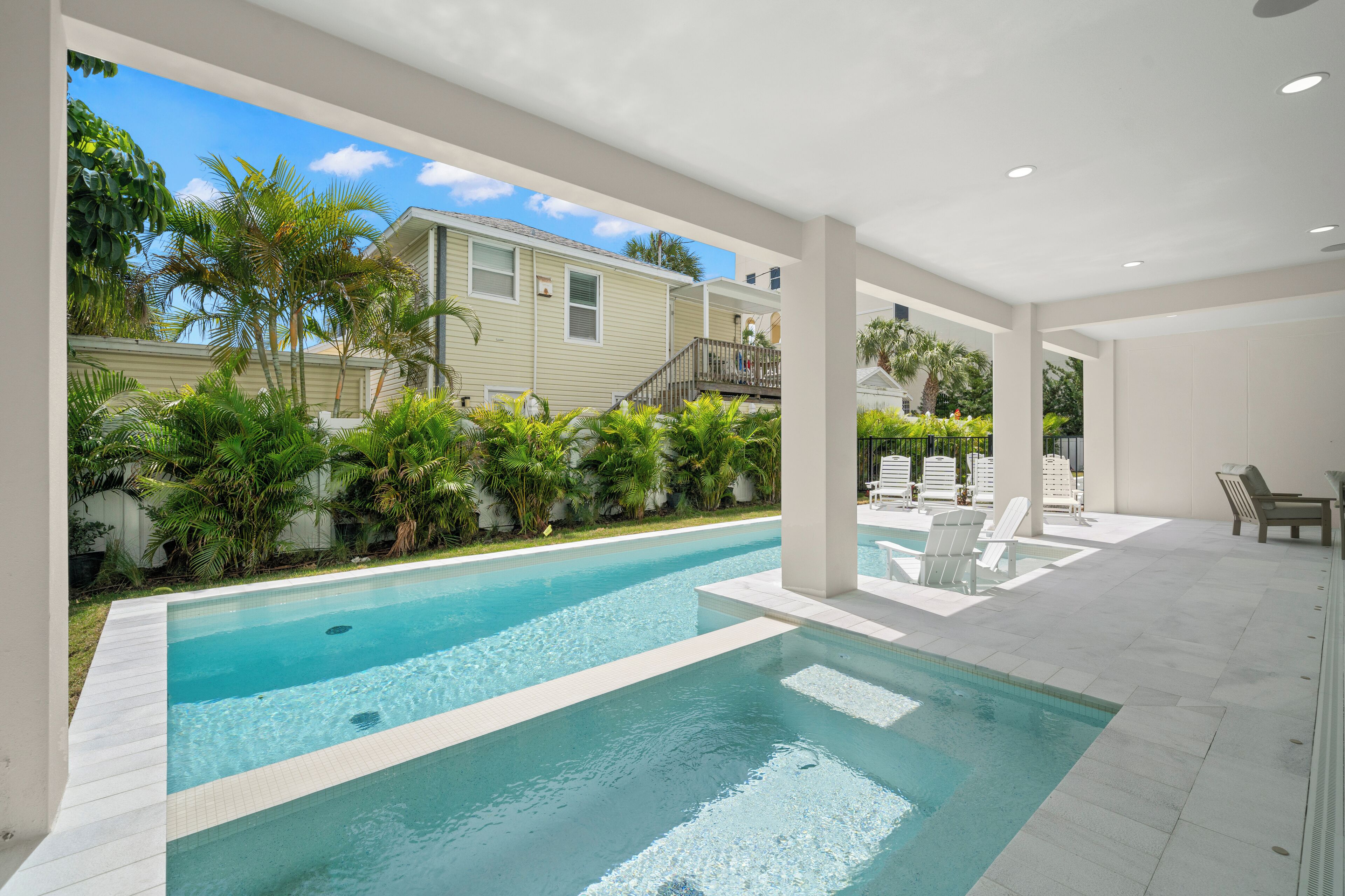 A swimming pool with clear blue water, surrounded by lush greenery and white lounge chairs.