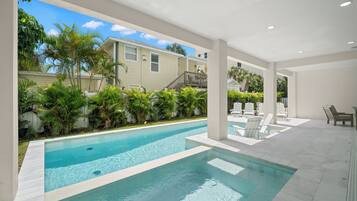 A swimming pool with clear blue water, surrounded by lush greenery and white lounge chairs.