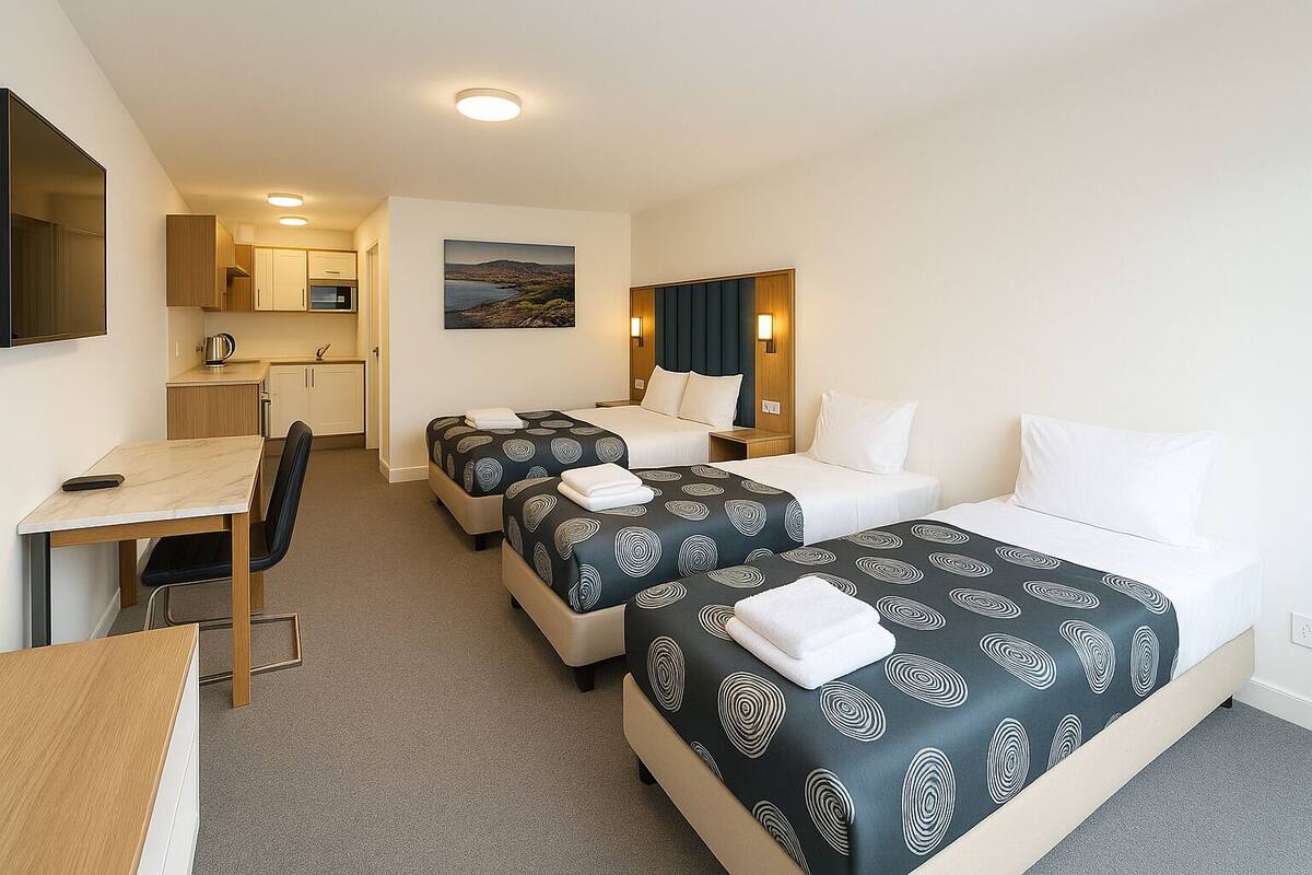 A hotel room with two beds, a desk, and a kitchenette.