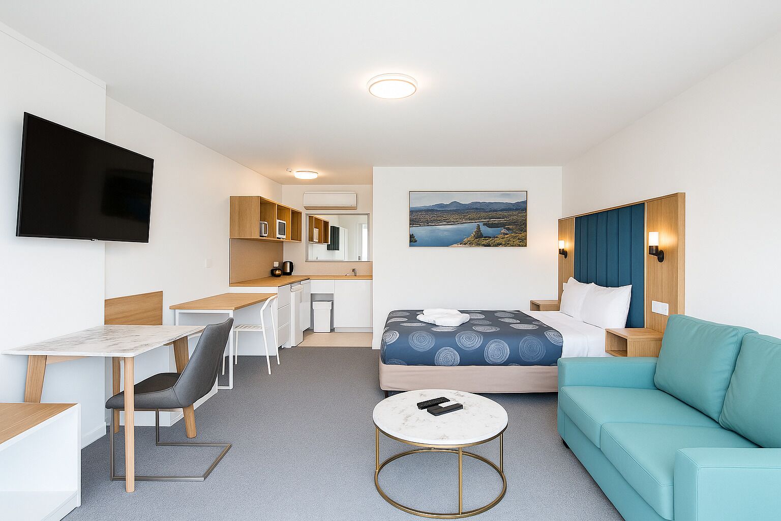 A compact hotel room with a bed, a sofa, a desk, and a TV.