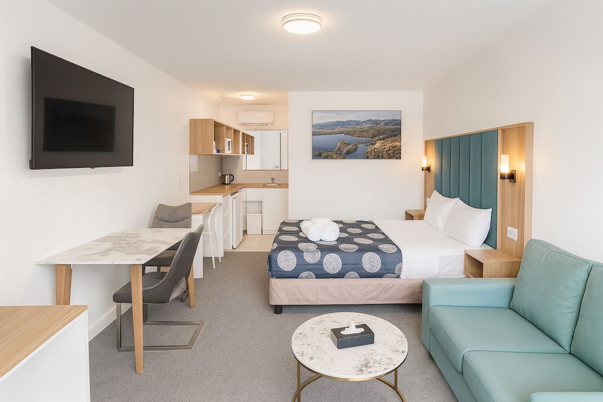 A compact hotel room with a bed, a sofa, a small table, a desk, and a TV.