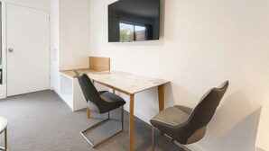 A modern, minimalist room with a white door, a flat-screen TV mounted on the wall, a marble-topped table, two black chairs, and a small wooden desk. - Eildon Lake Motel (Eildon)