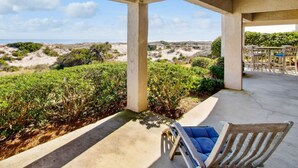 Un espace extérieur abrité, avec vue sur la plage et les dunes, comprenant un coin salon avec des chaises et une table.