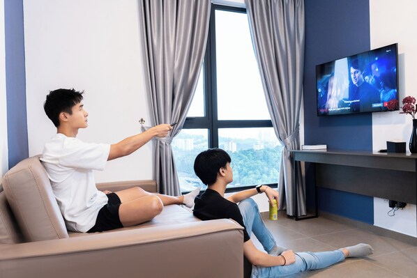 Two people sitting on a sofa watching TV in a room with a large window and a flat-screen TV mounted on the wall.