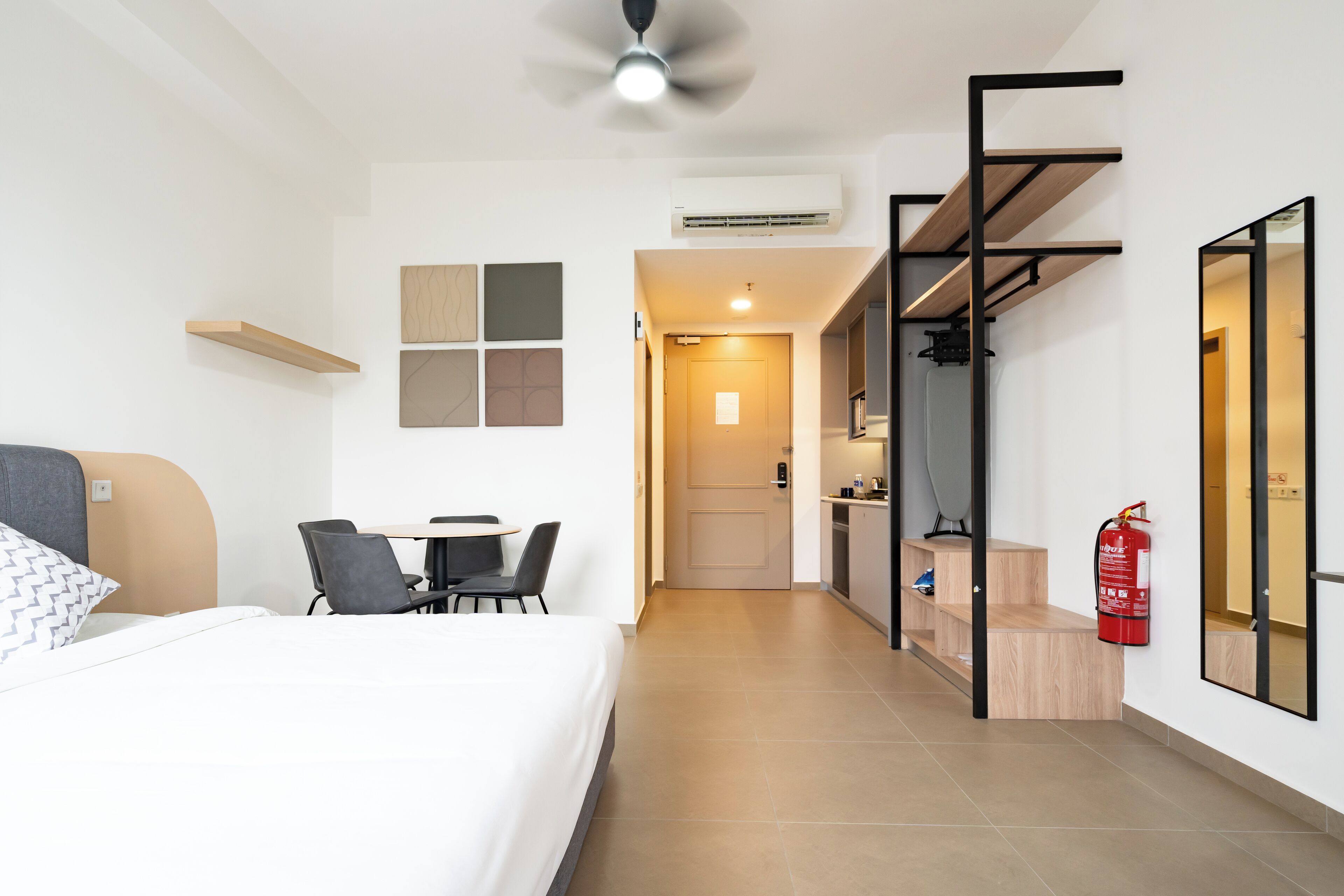 A modern hotel room with a bed, desk, chairs, and a kitchenette.