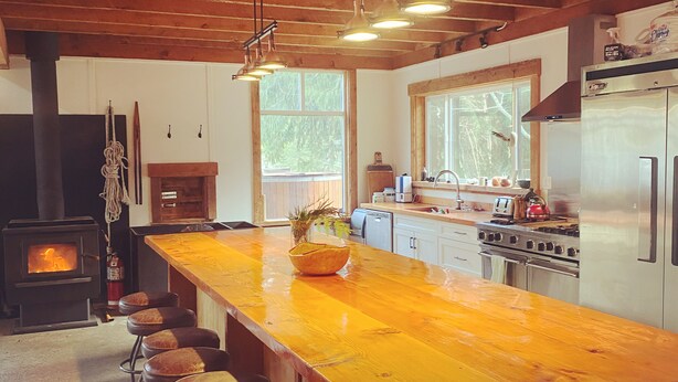 A kitchen with a wooden island, bar stools, a stove, and a refrigerator. - "Sleeps 15: Dog-Friendly Rustic Haven on Cortes Island" Large grass yard (Mansons Landing)