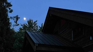 A rustic cabin with a stone foundation, a metal roof, and a lit interior visible through large windows. - "Sleeps 15: Dog-Friendly Rustic Haven on Cortes Island" Large grass yard (Mansons Landing)