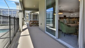 Un salon moderne doté d’une porte vitrée donnant sur un balcon, d’un fauteuil vert et d’un coin repas avec une table et des chaises.