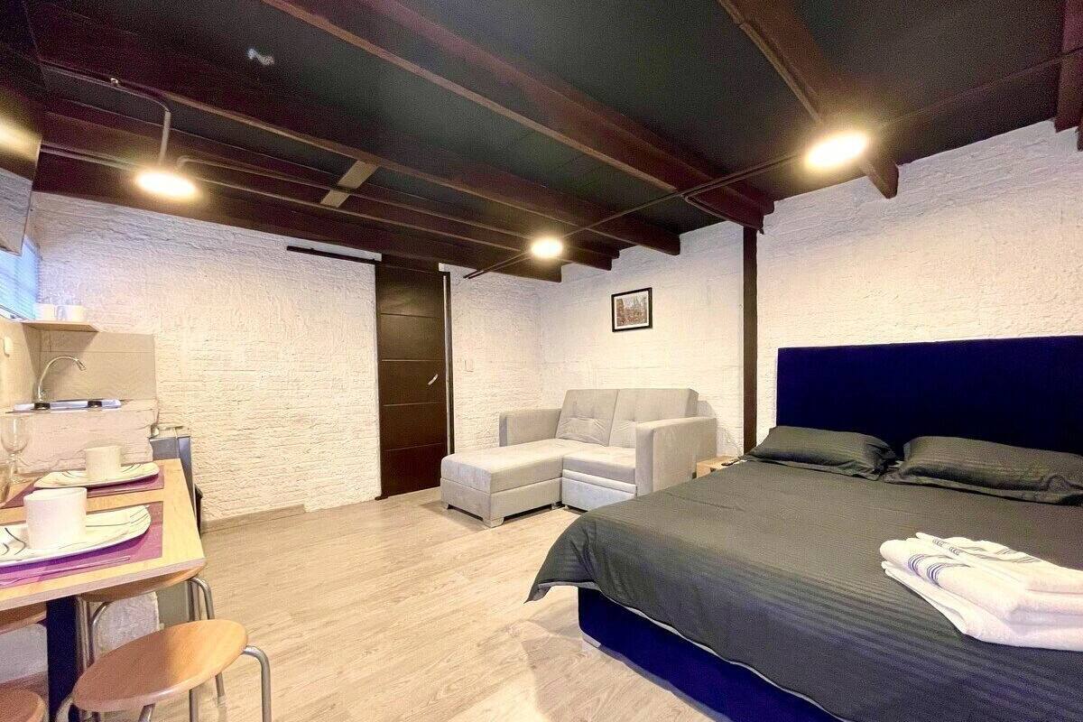 A modern bedroom with a bed, a sofa, a desk with a chair, and a small table.