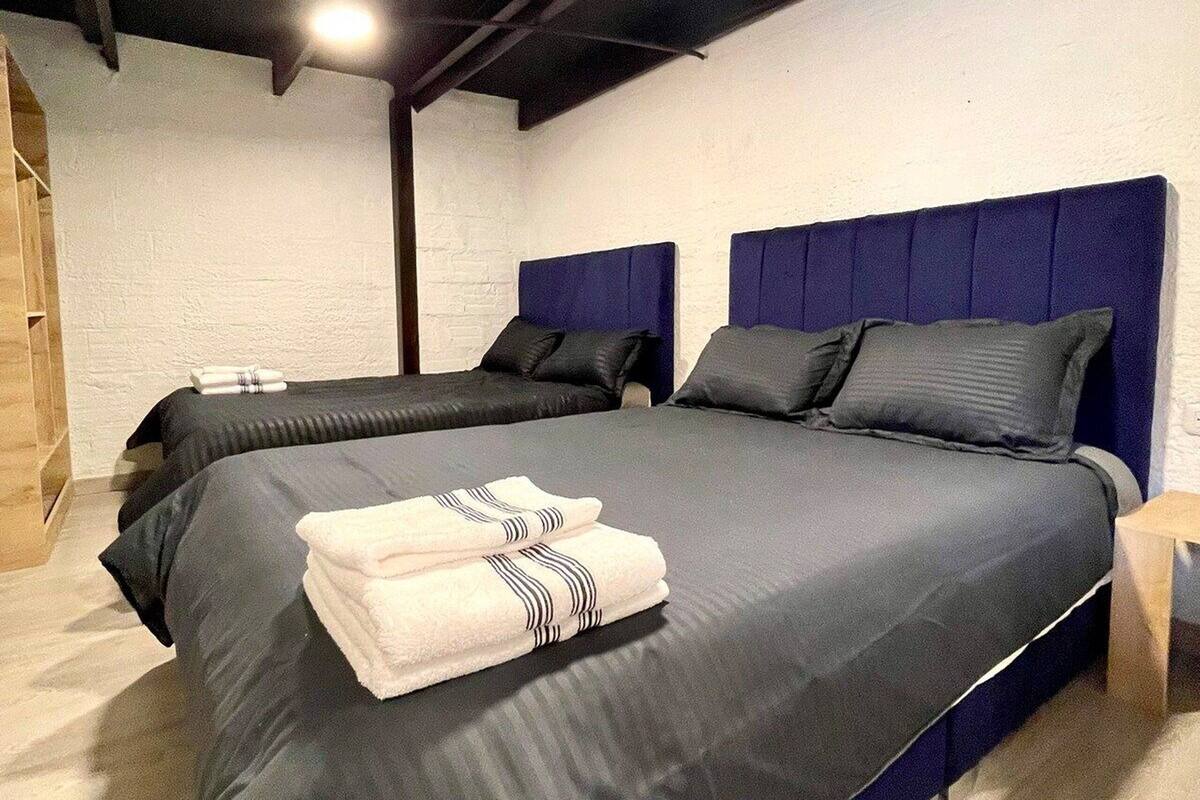 A modern bedroom with a large bed, dark headboard, and a wooden floor.