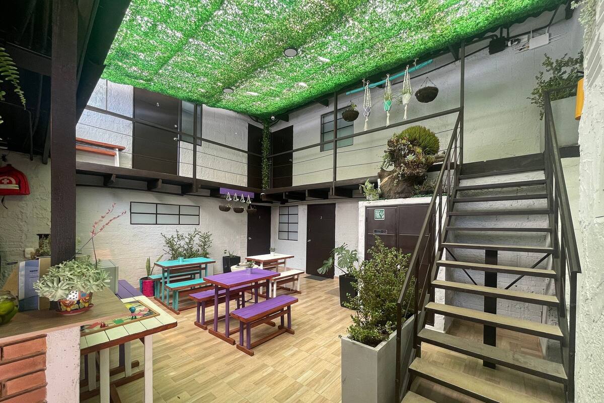 An indoor space with a wooden floor, tables, benches, and potted plants.