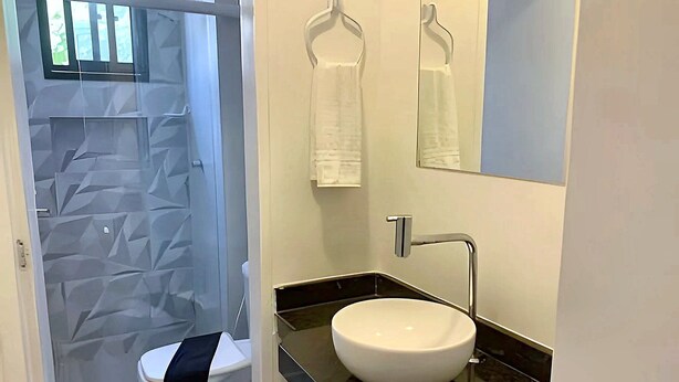 A bathroom with a white toilet, a black sink, a mirror, and a towel rack. - Hosts BR - Apartamentos funcionais (Fortaleza)