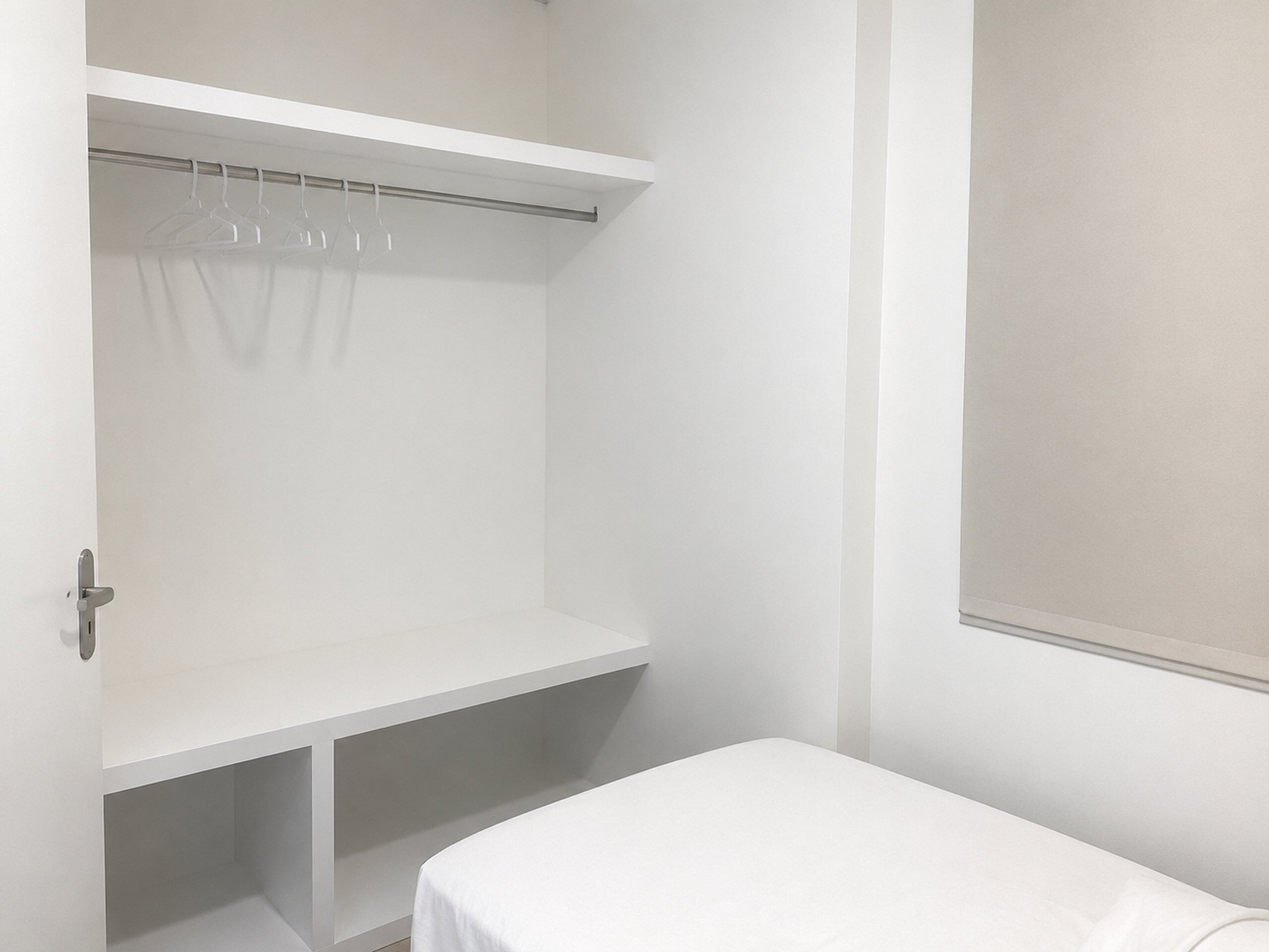 A white room with a bed, a closet with hanging space, and a window.