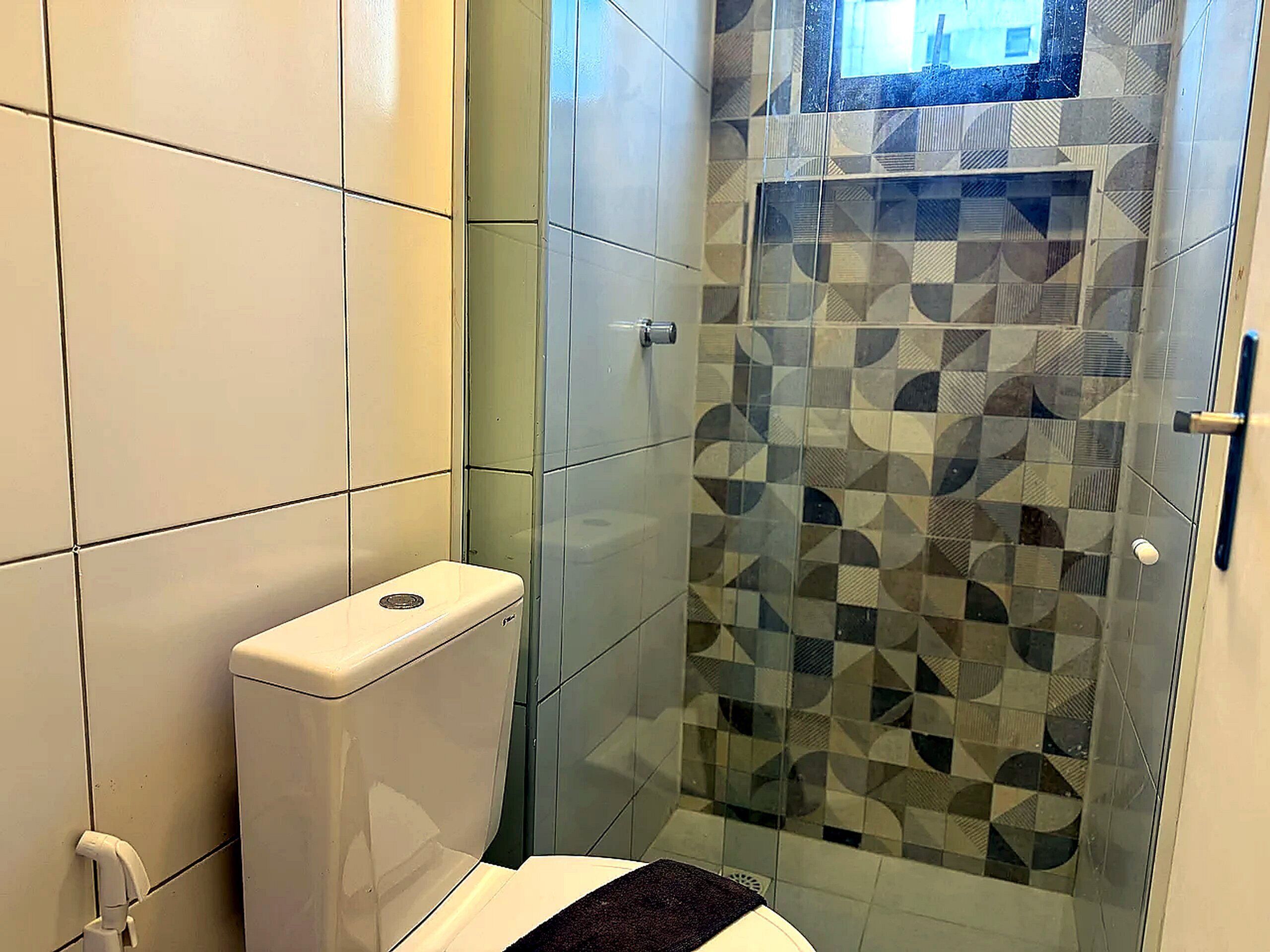 A bathroom with a toilet, a glass shower enclosure, and tiled walls.