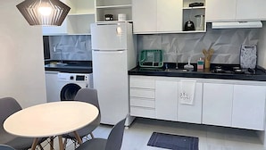 Une cuisine compacte équipée d’un lave-linge, d’une table à manger avec des chaises et d’un luminaire suspendu.