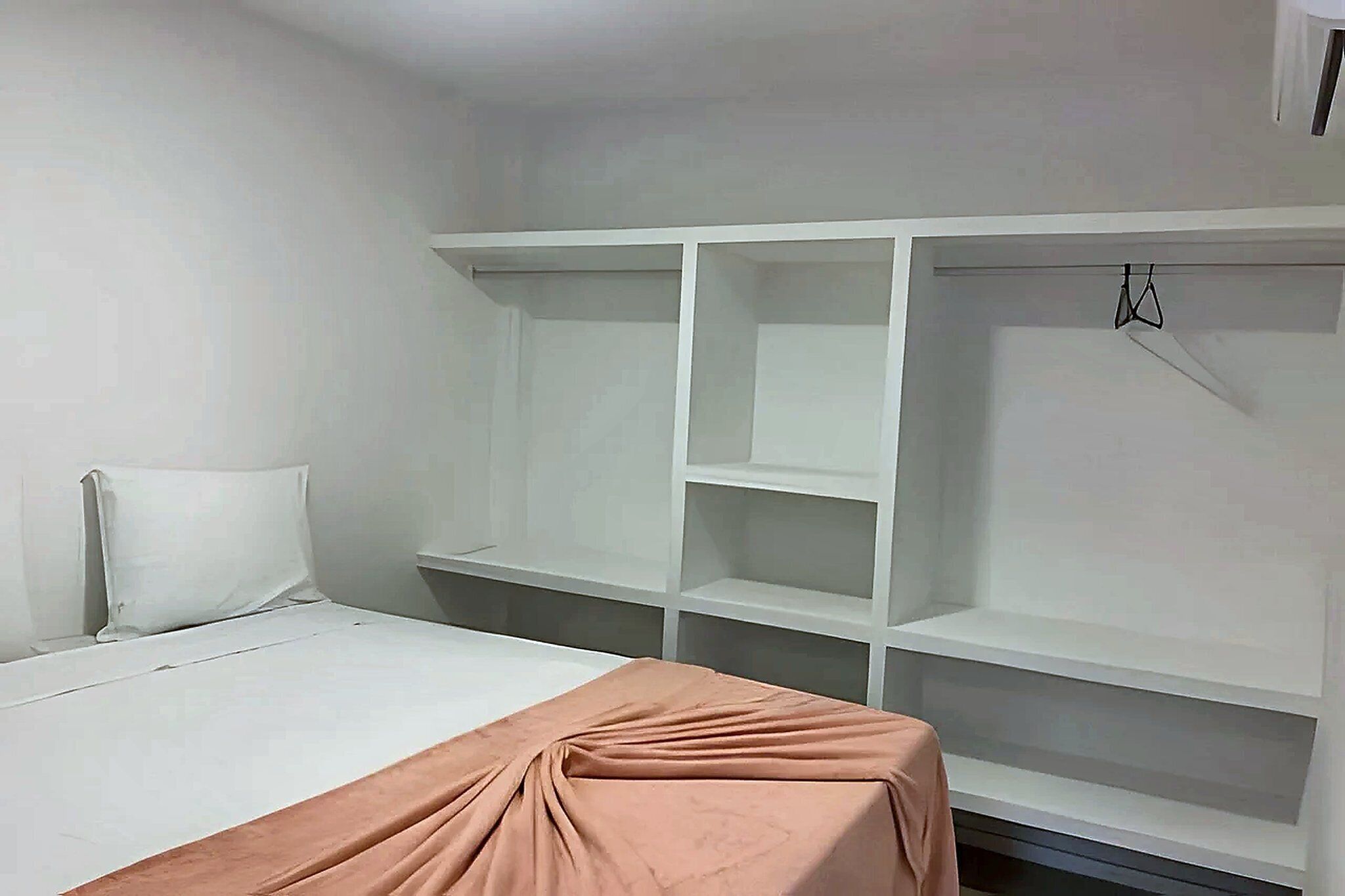 Une chambre à coucher comprenant un lit, une armoire avec plusieurs étagères et une tringle pour suspendre les vêtements.