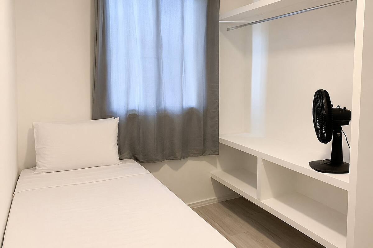 Quarto com cama, janela com cortinas, ventilador e guarda-roupa branco.