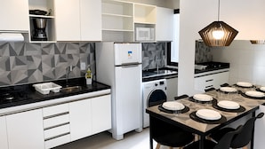 Une cuisine moderne avec des meubles blancs, un lave-linge encastré, un four à micro-ondes et un coin repas avec une table dressée pour quatre personnes.