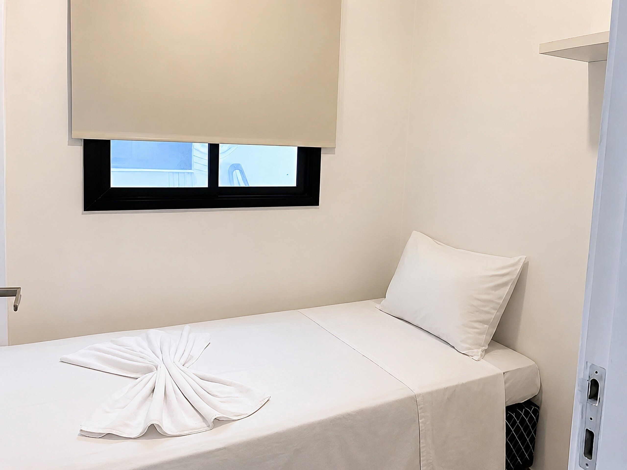 Un lit simple avec une couverture blanche et une serviette, une fenêtre donnant sur un paysage agréable et un mur blanc.