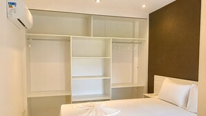 Une chambre d’hôtel avec un grand lit blanc, une armoire avec plusieurs étagères et une table de chevet.