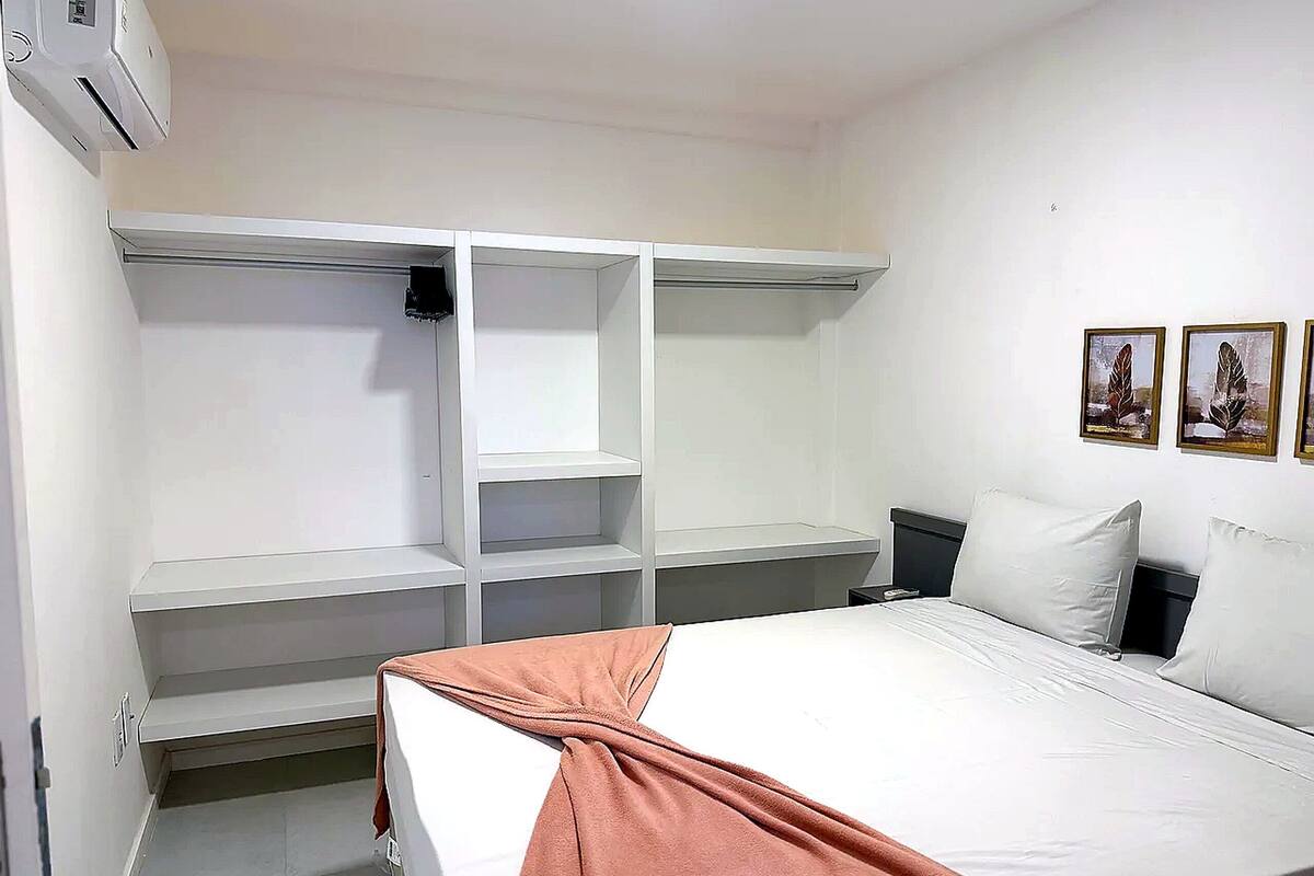 Quarto com cama, guarda-roupa, mesa de cabeceira e ar condicionado fixado na parede.
