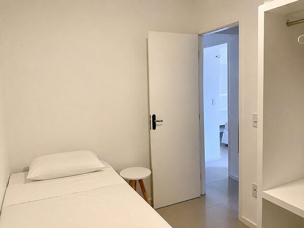 Un dormitorio minimalista con una cama individual, una mesita redonda pequeña y una puerta que da a un baño.