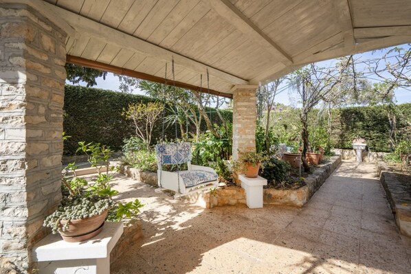 A covered outdoor area with stone pillars, a seating area, and potted plants.