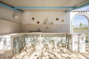 A kitchen with a tiled backsplash, a gas stove, and a sink. There are decorative plates on the wall and a window with a view of trees.
